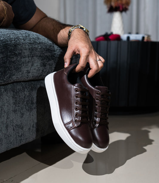 Person holding a pair of brown leather sneakers with white soles.