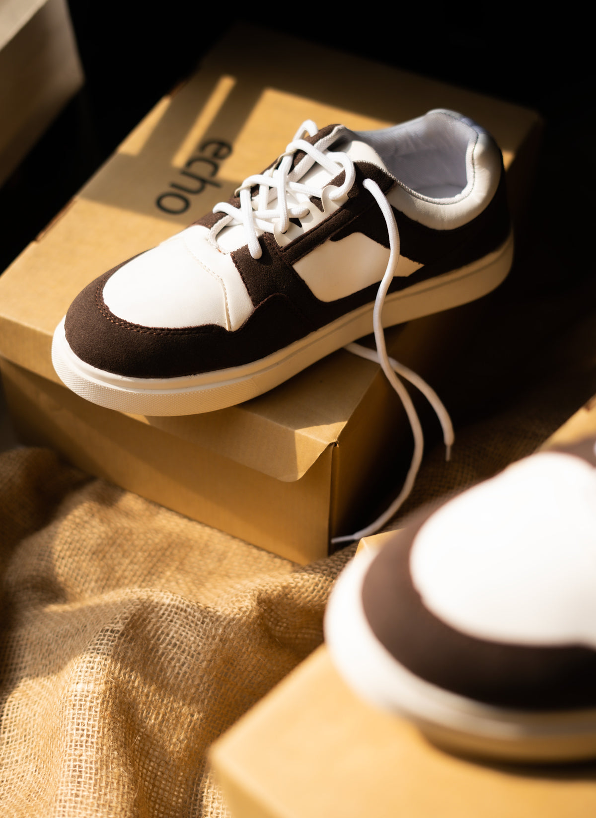 BROWN and white sneakers on a cardboard box with a textured fabric background