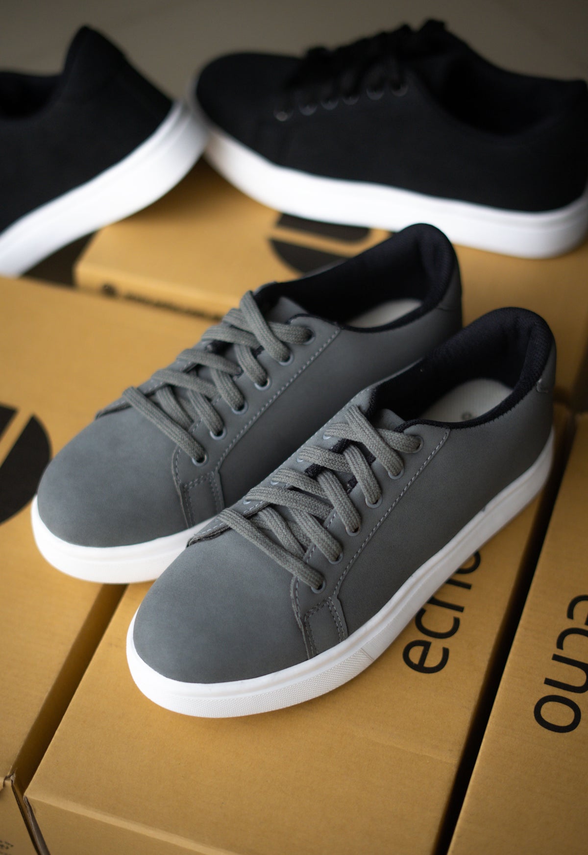 Gray sneakers on a cardboard box with black sneakers in the background