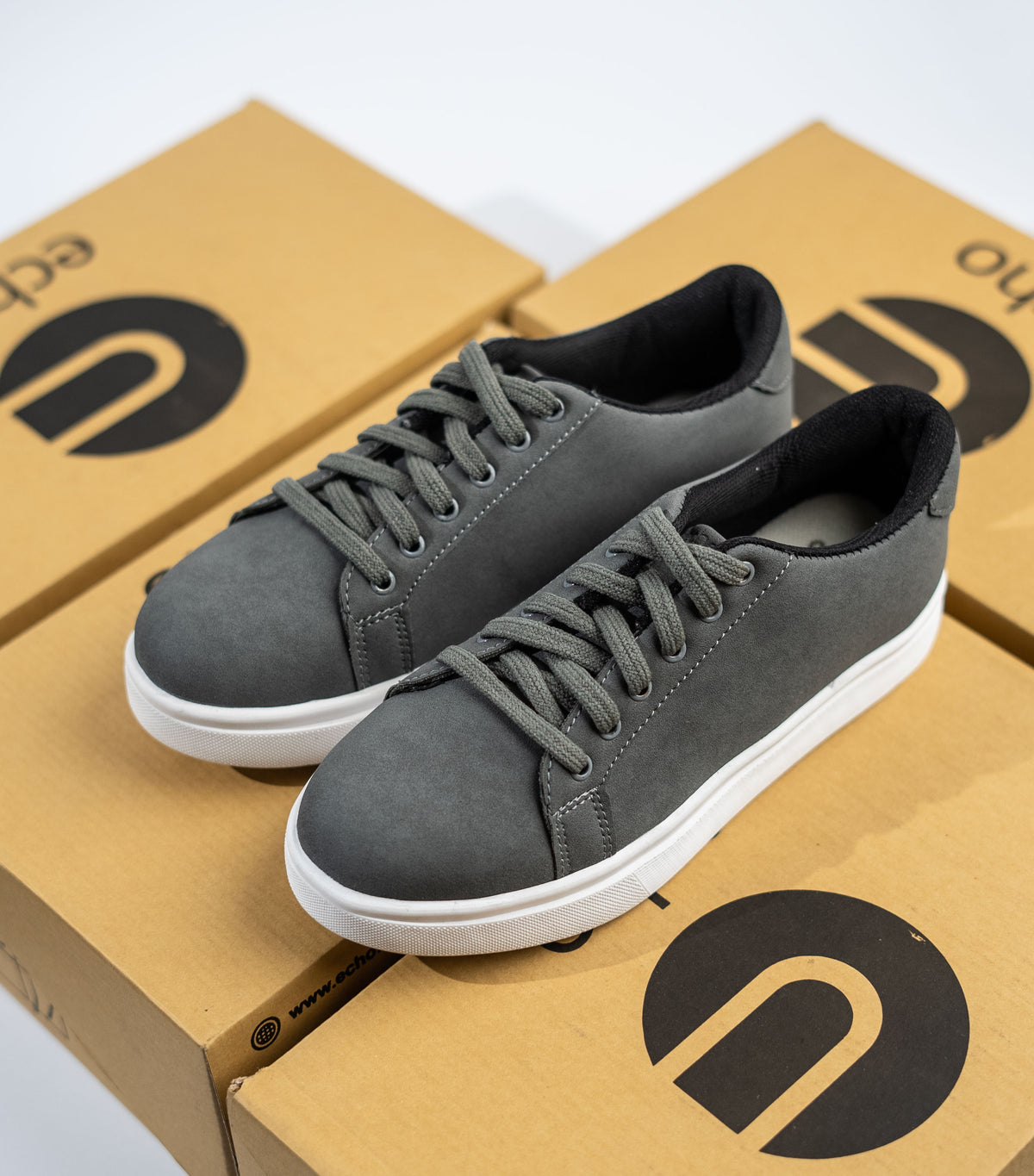 Gray sneakers with white soles on a cardboard box with a ECHO logo.