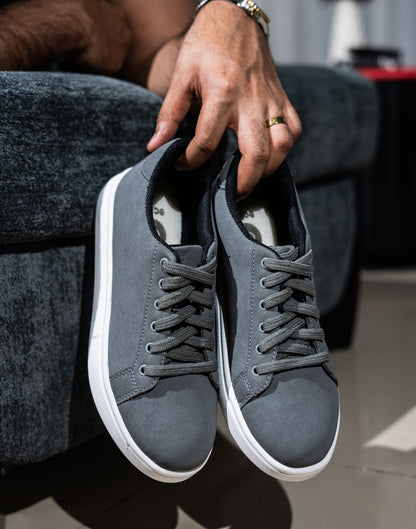 Person holding a pair of gray sneakers with white soles.